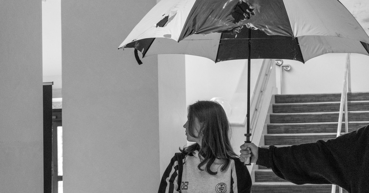 A person stands indoors holding a damaged umbrella in a black and white setting.