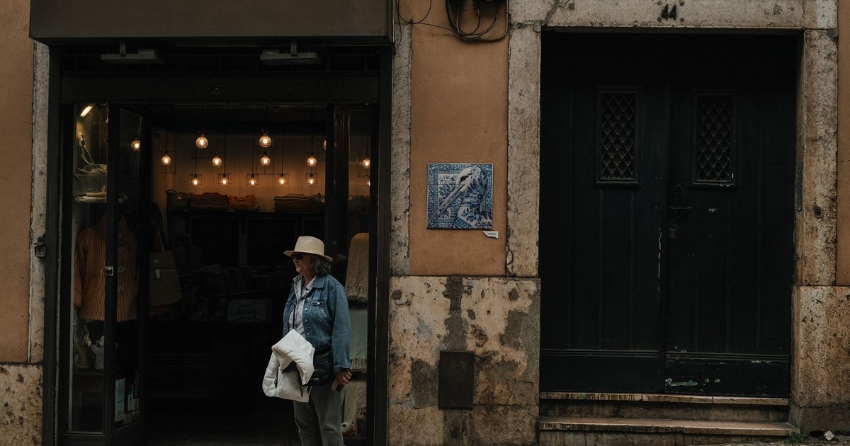 Elderly woman stands by a quaint storefront with vintage lighting, capturing a calm urban moment.