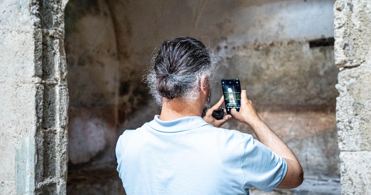 A man uses a smartphone to photograph ancient ruins indoors, capturing history through technology.
