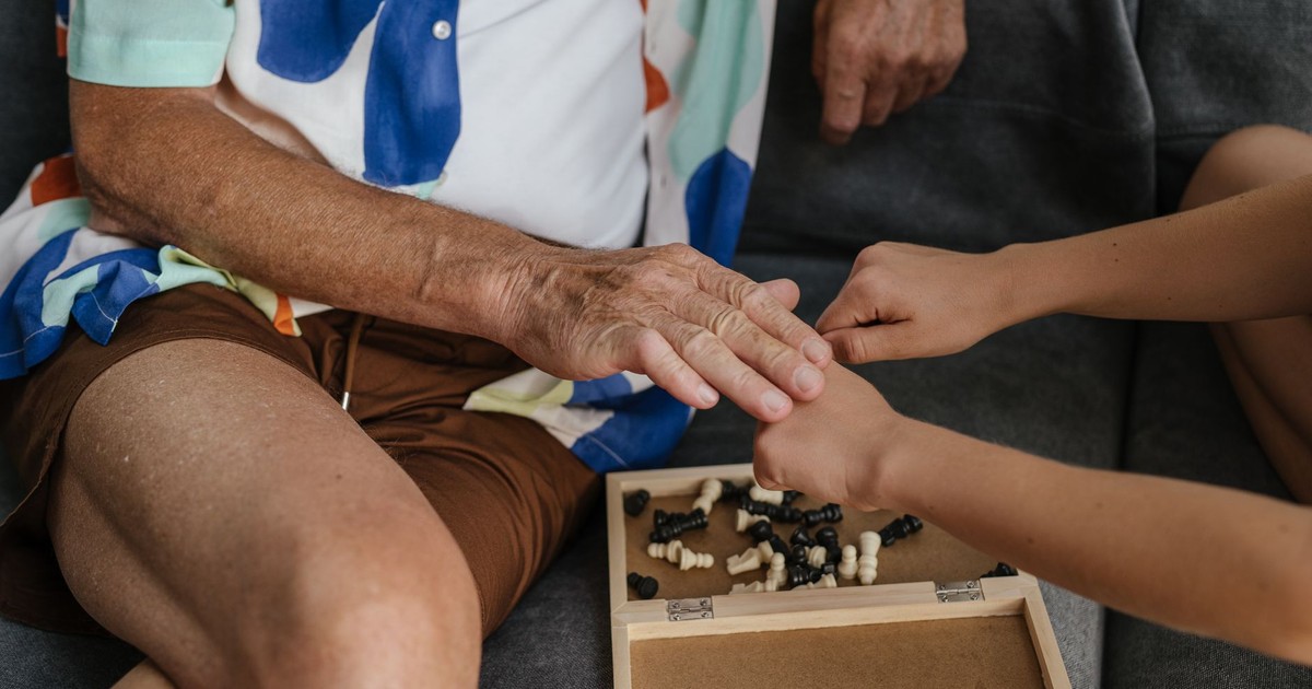 An elderly person and child play chess indoors, focusing on hands with chess pieces.