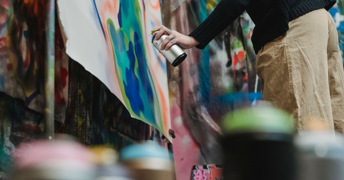 Artist using spray paint to create vibrant graffiti on canvas indoors.