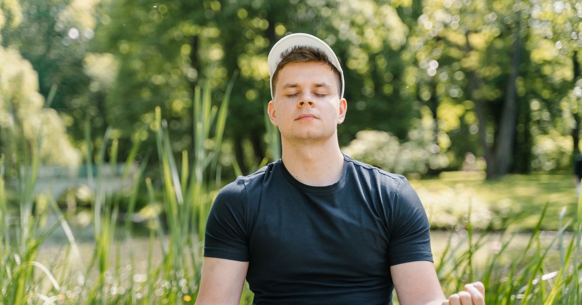 Man in black shirt meditates peacefully in a lush green park, eyes closed in relaxation