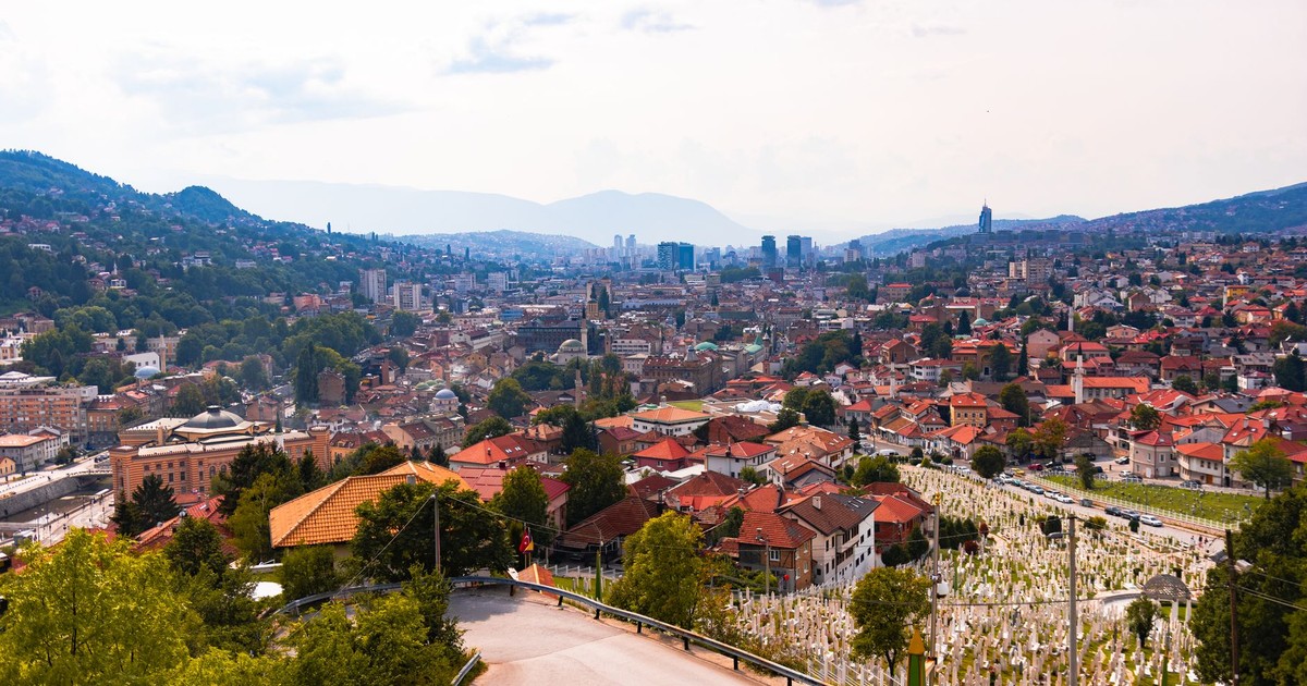 Aerial view of Sarajevo, showcasing cityscape, red rooftops, and distant mountains.