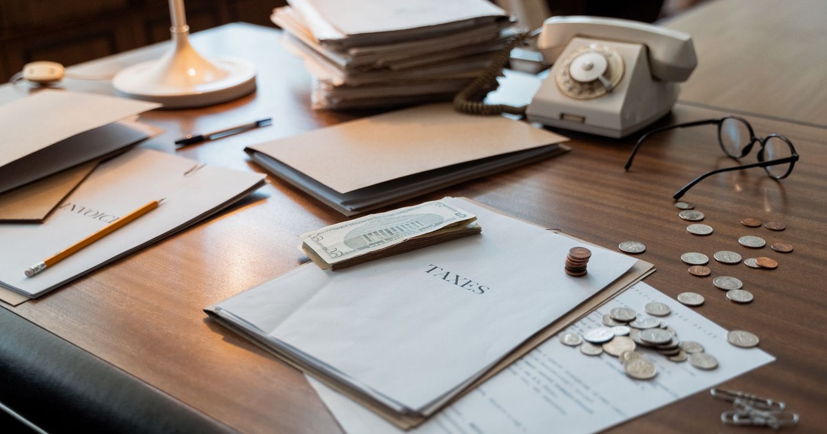Close-up of an office desk with tax documents, coins, glasses, and an old phone, symbolizing finance and organization.