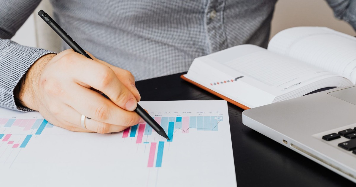 A business analyst examines a graph on paper with a laptop and notebook indoors.