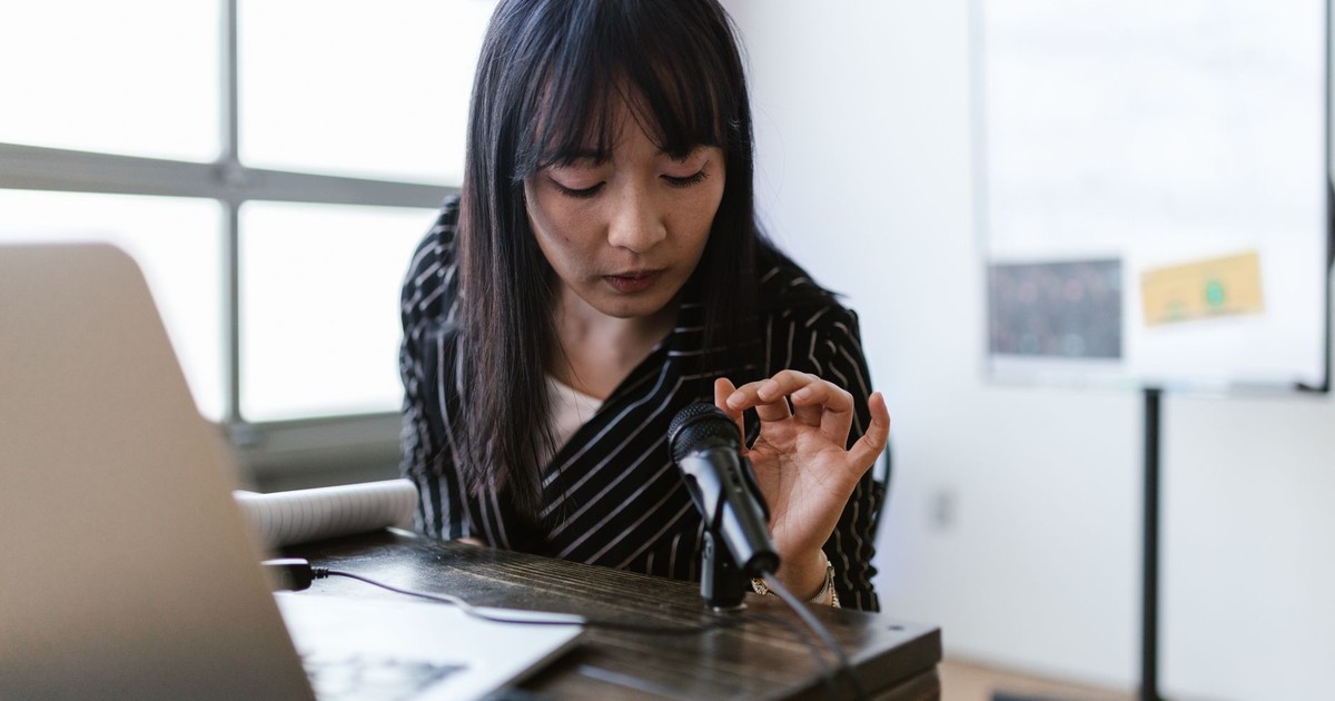 A woman in an office setting testing a microphone while sitting at a desk with a laptop.
