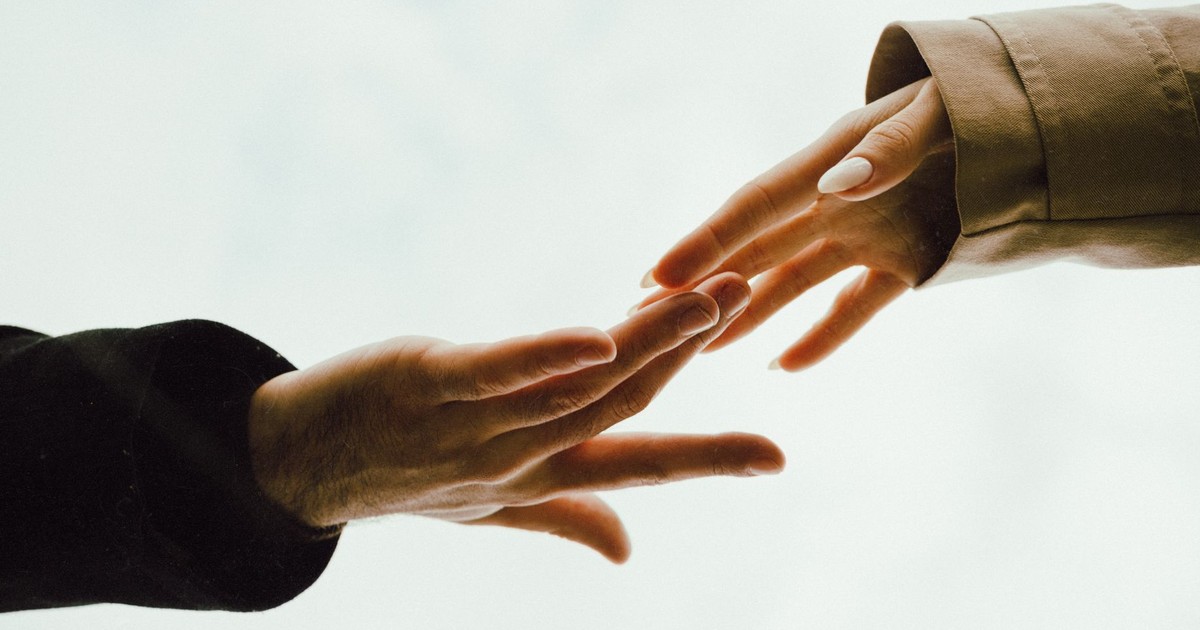 A tender moment captured as two hands reach out towards each other with a soft background.