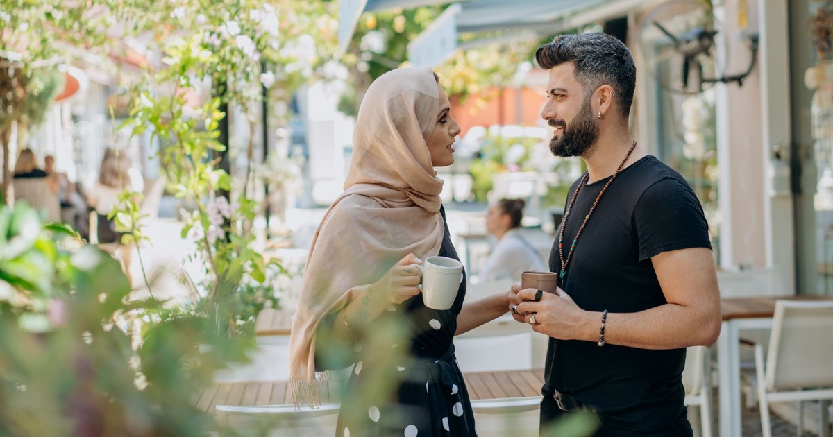 A couple enjoying coffee outside a sunlit cafe, engaging in a lively conversation and sharing a joyful moment together.