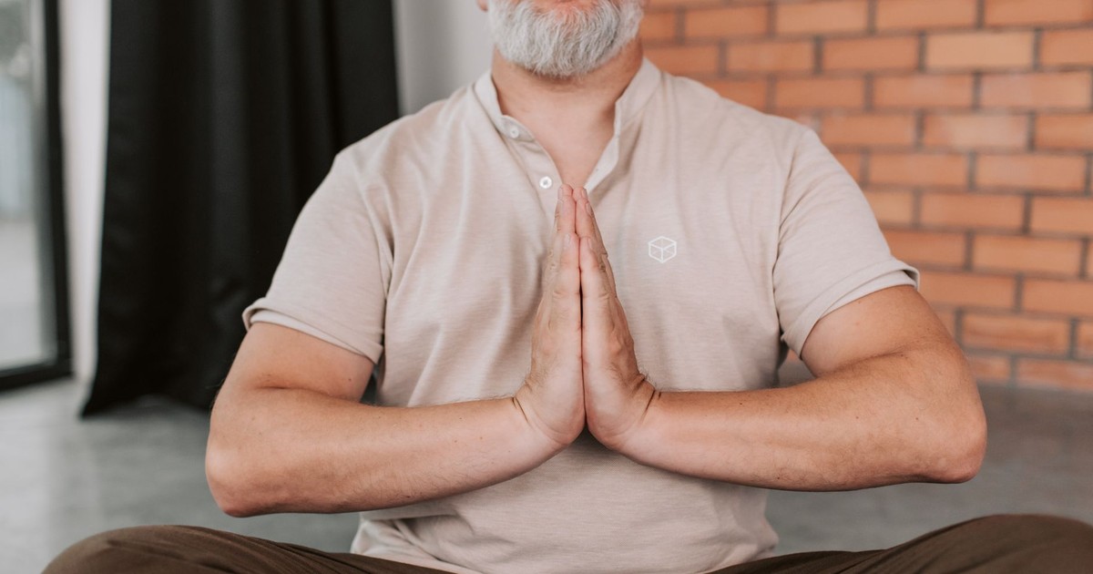 Senior man practicing meditation with hands in prayer pose inside a calm setting.