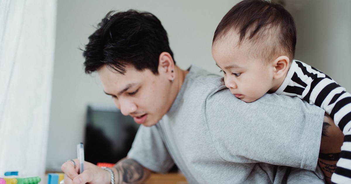 A father multitasking work while carrying his child, highlighting parenthood challenges.