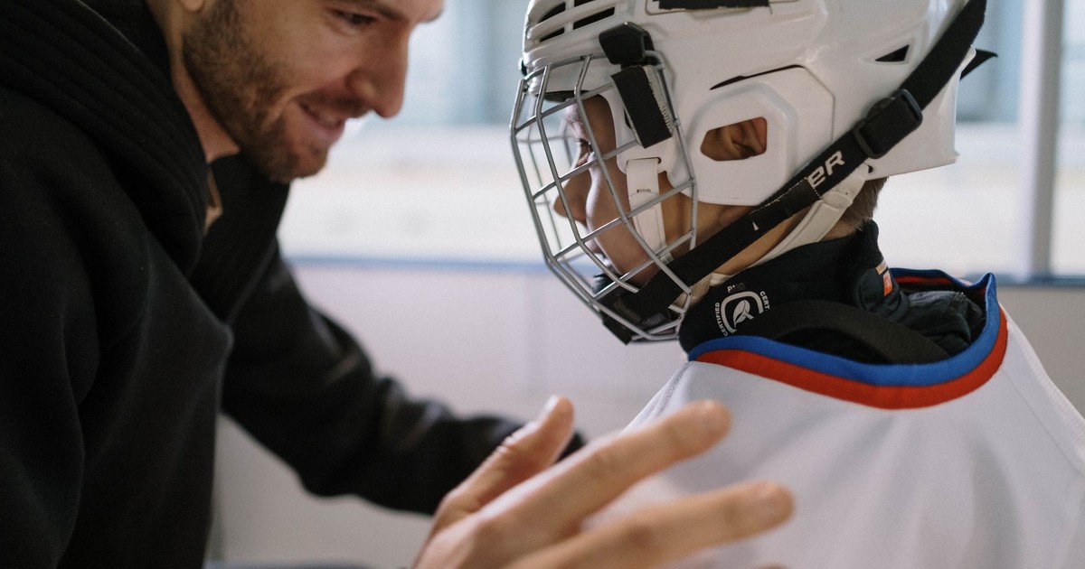 Father and son bonding moment before an ice hockey game, with the boy in his white jersey and helmet.