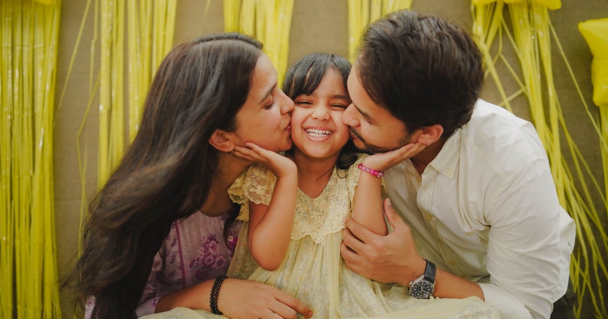 A heartwarming family moment with parents kissing their daughter during a festive celebration.