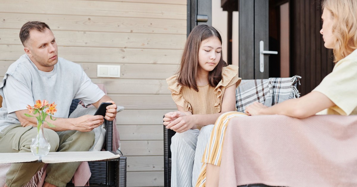 A family of three having a serious conversation outdoors on a patio.