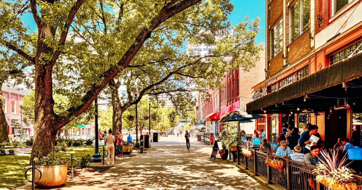 Vibrant street scene in Knoxville, Tennessee with people enjoying outdoor dining under tree shade.