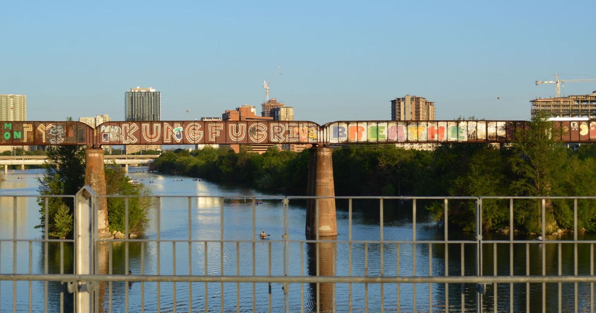 Colorful graffiti on a bridge over Lady Bird Lake with Austin skyline in the backdrop.