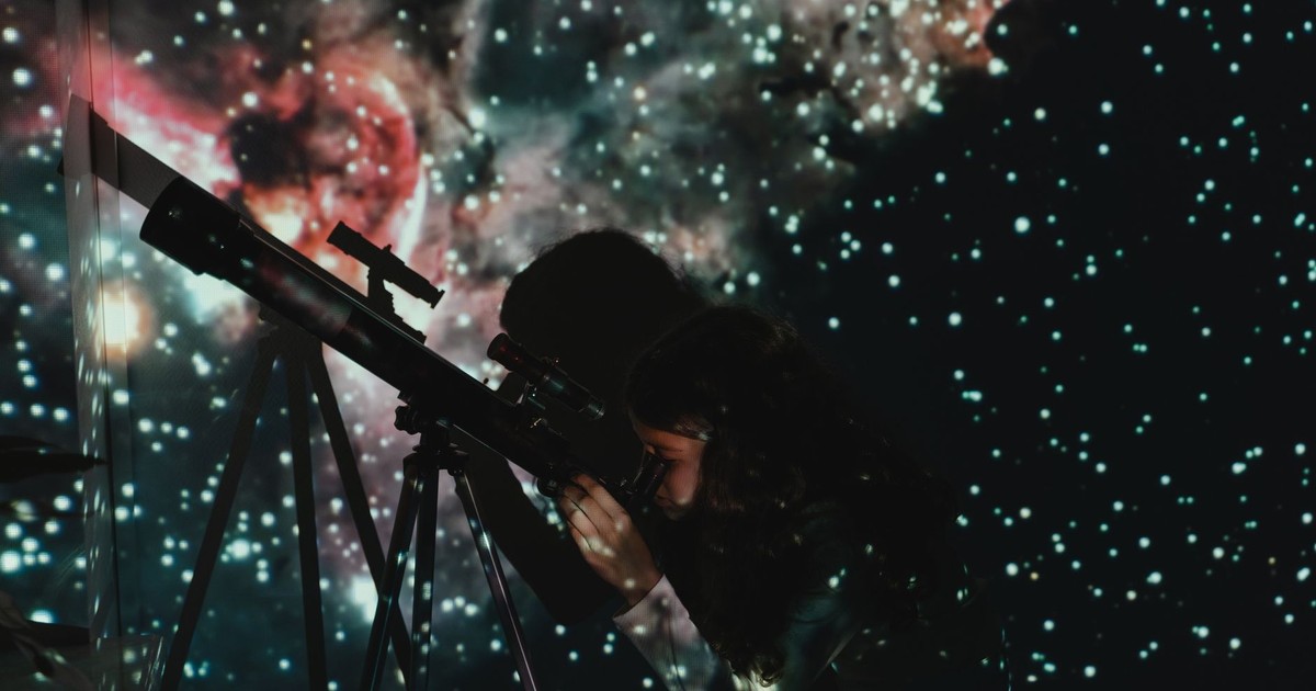 A girl looks through a telescope at a starry projection, blending education with wonder.
