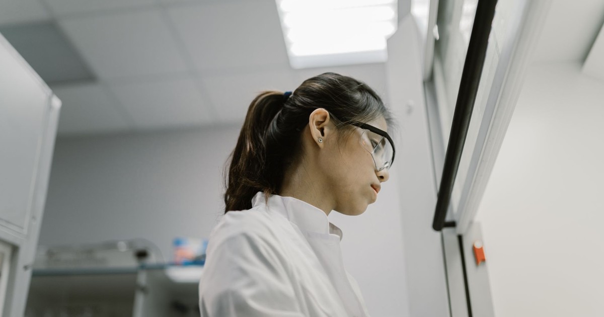 Asian woman scientist wearing protective goggles conducting research in a modern lab.