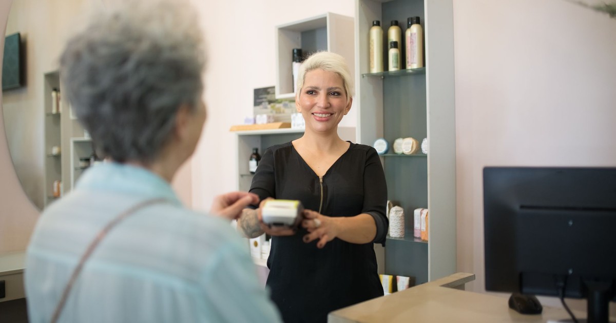 Friendly hairdresser assisting customer with payment in a stylish salon setting.
