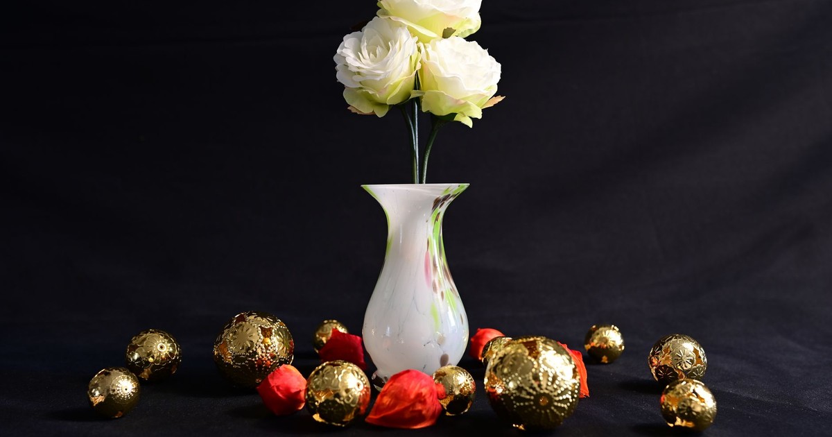 White roses in a vase surrounded by golden and red ornaments, perfect for decoration themes.