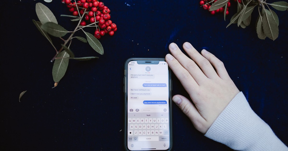 A hand beside a smartphone showing a text message conversation, surrounded by red berries.