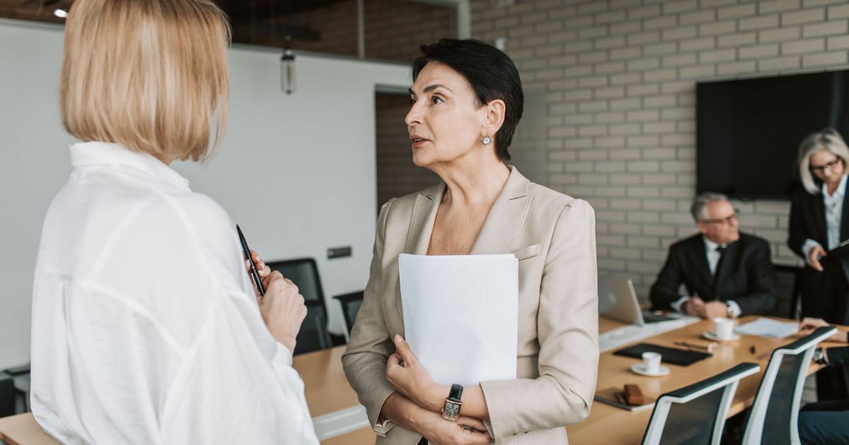 Two businesswomen engage in a conversation during a professional meeting in a modern office.
