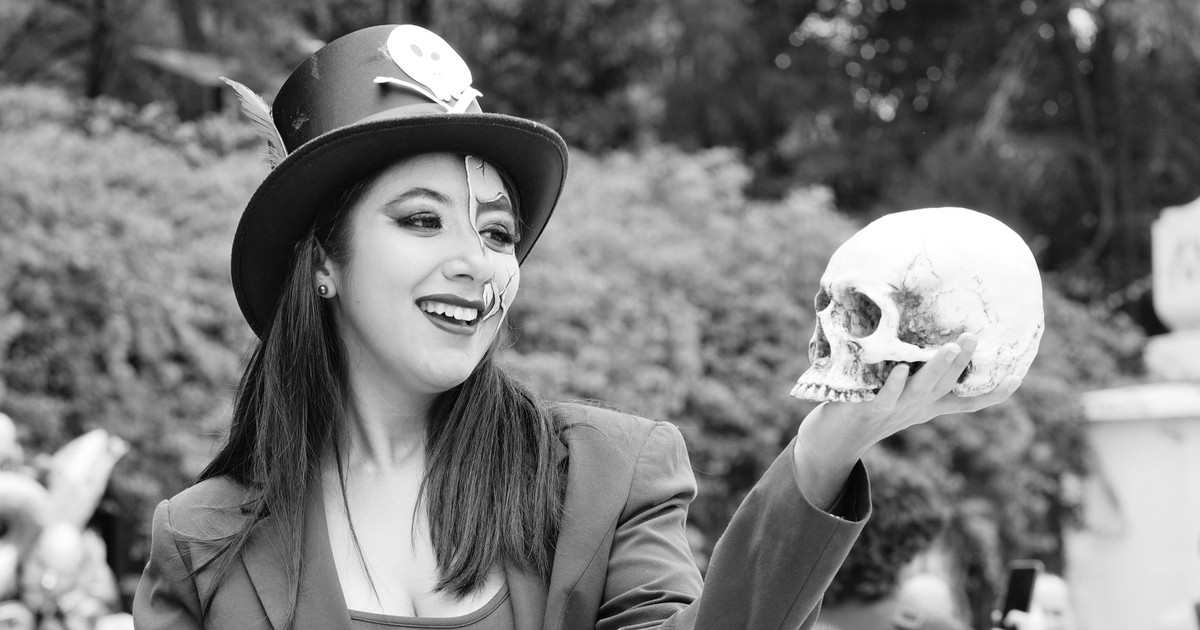 Woman with face paint and skull embracing Day of the Dead celebration with joy.