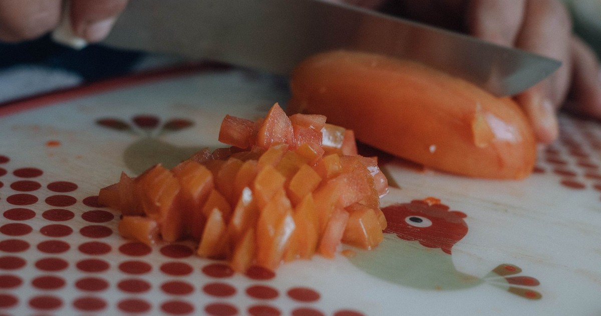 Hands chopping a tomato on a decorative cutting board in a kitchen setting.