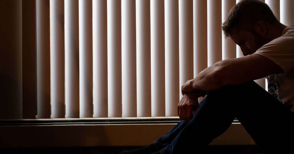 A man sits silhouetted against window blinds, conveying solitude and introspection.