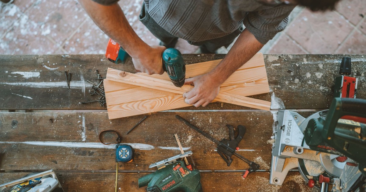 Craftsman busy drilling wooden planks in a carpentry workshop with various tools around.