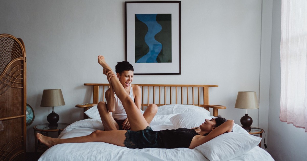 Two women having fun and laughing together in a cozy bedroom setting.