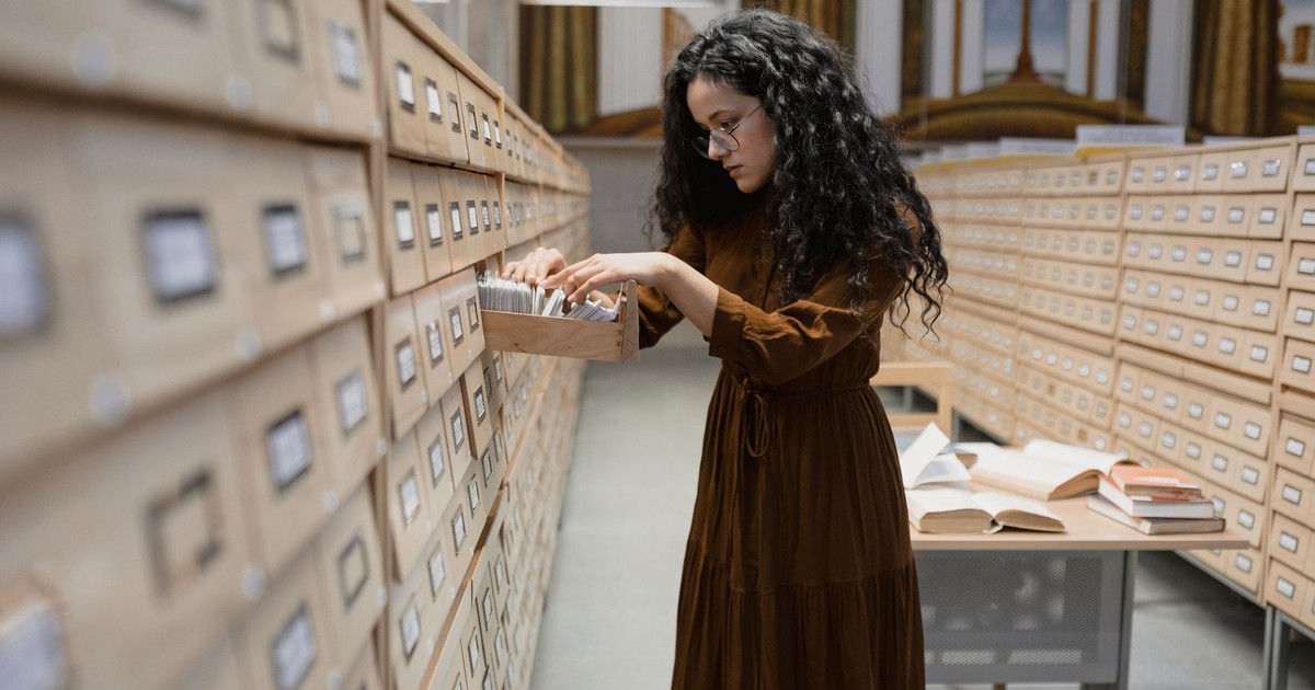 A woman browsing a card catalog in library archives, focusing on research and information gathering.