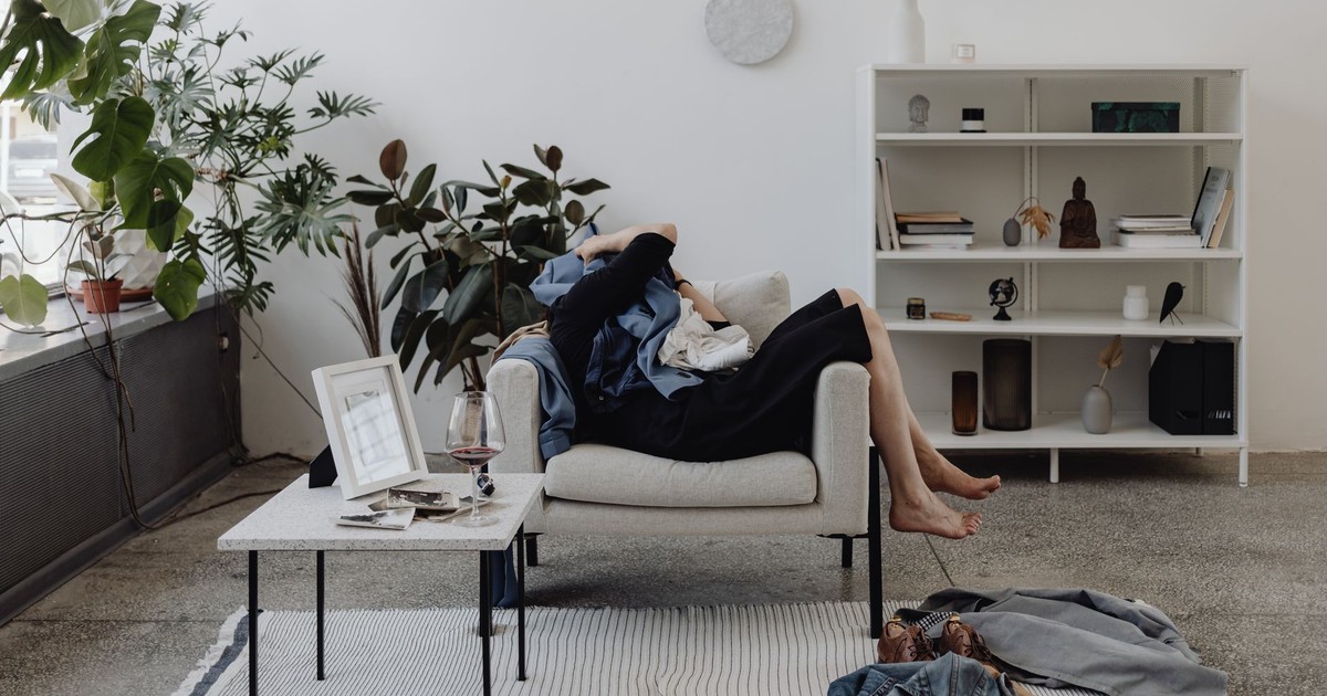 A person resting on a sofa in a cozy living room with plants and a glass of wine.