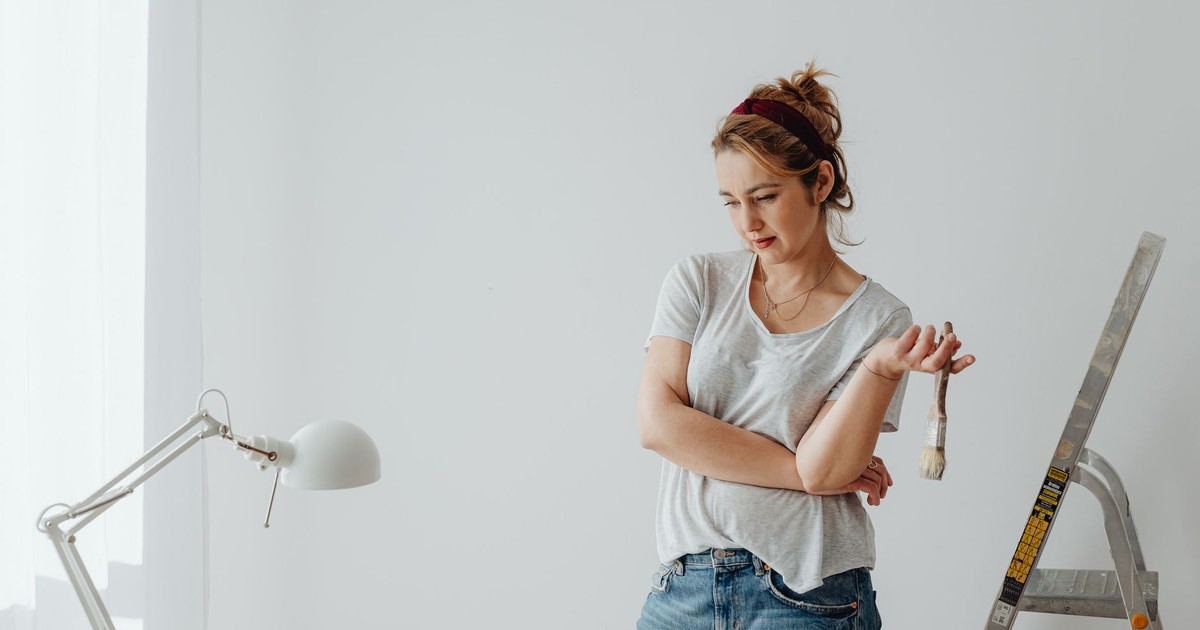 Young woman in casual attire pondering a home DIY project with paintbrush.