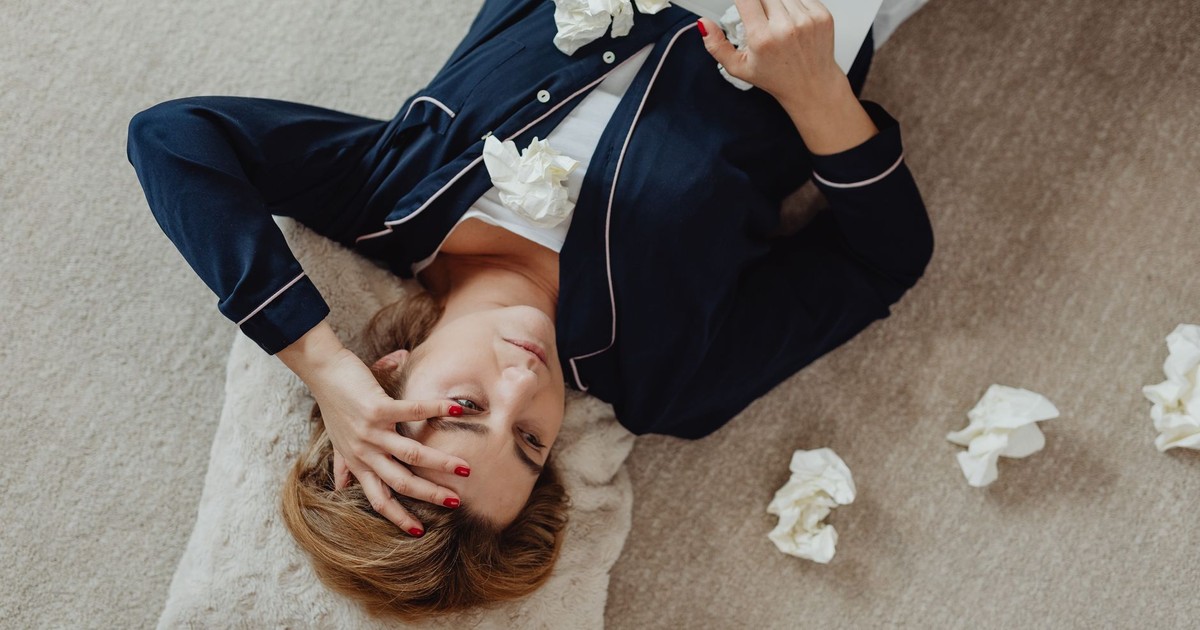 A woman in pajamas, stressed and lying on the floor with a laptop and scattered tissues.
