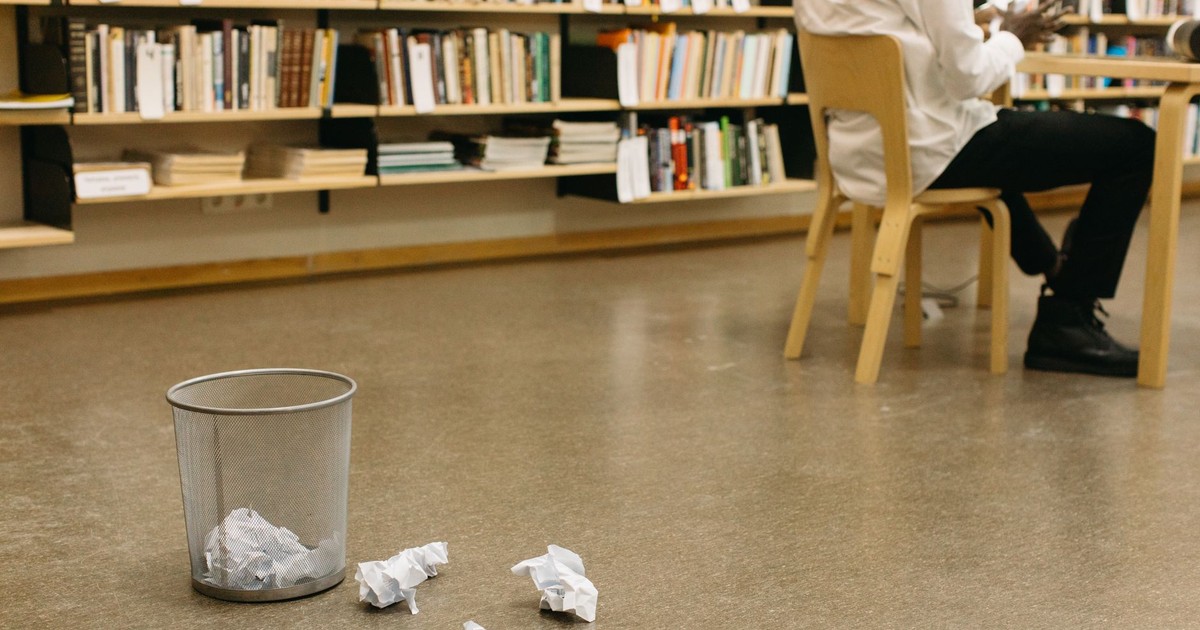 A library scene with crumpled papers near a trash can and a seated person, creating a thoughtful atmosphere.