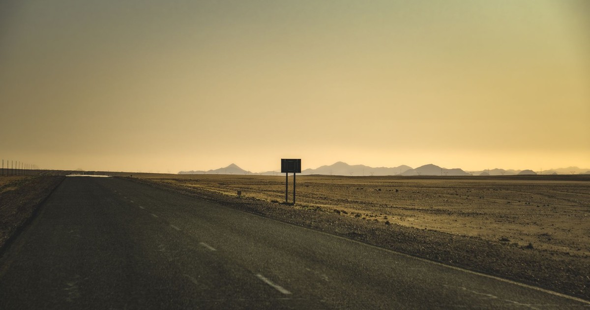 A serene view of an empty road stretching through a desert at sunset with distant mountains.