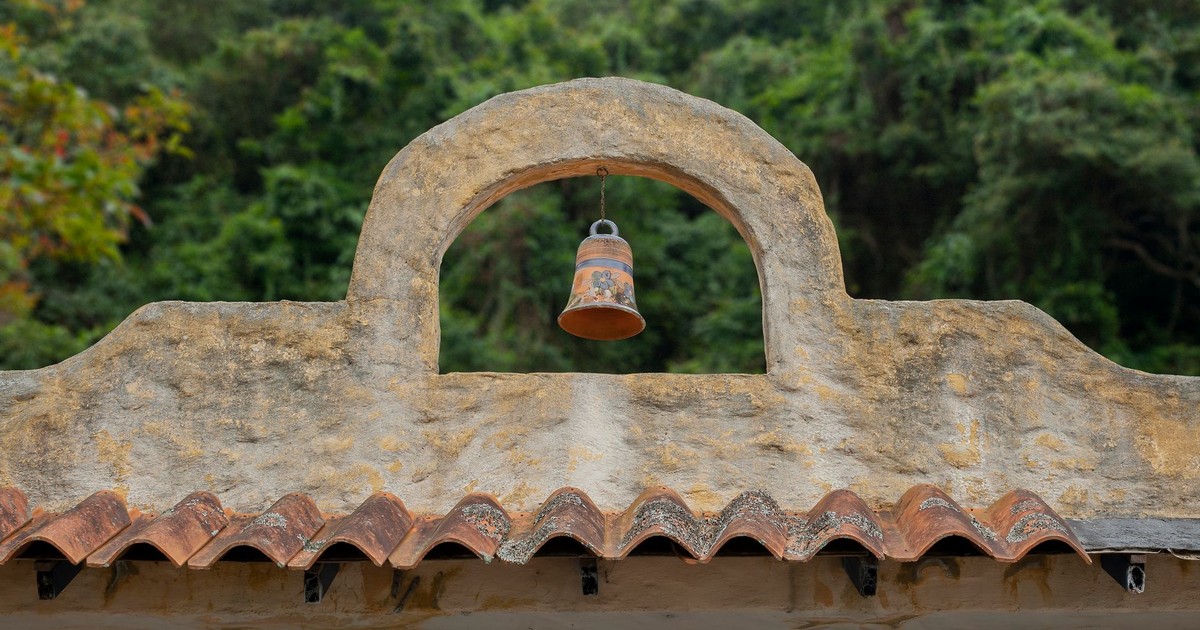 A colonial bell hangs on a rustic rooftop arch in Mérida, Venezuela, evoking a sense of history and tradition.