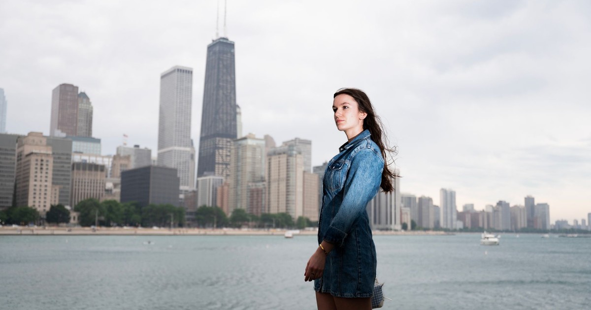 Young woman in denim jacket standing by Lake Michigan with Chicago skyline in the background.