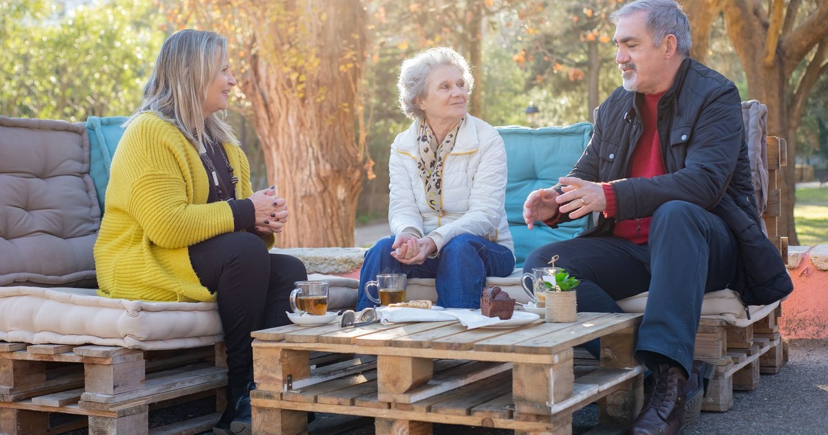 Group of seniors having tea and chatting in a sunny park, enjoying a relaxed moment together.