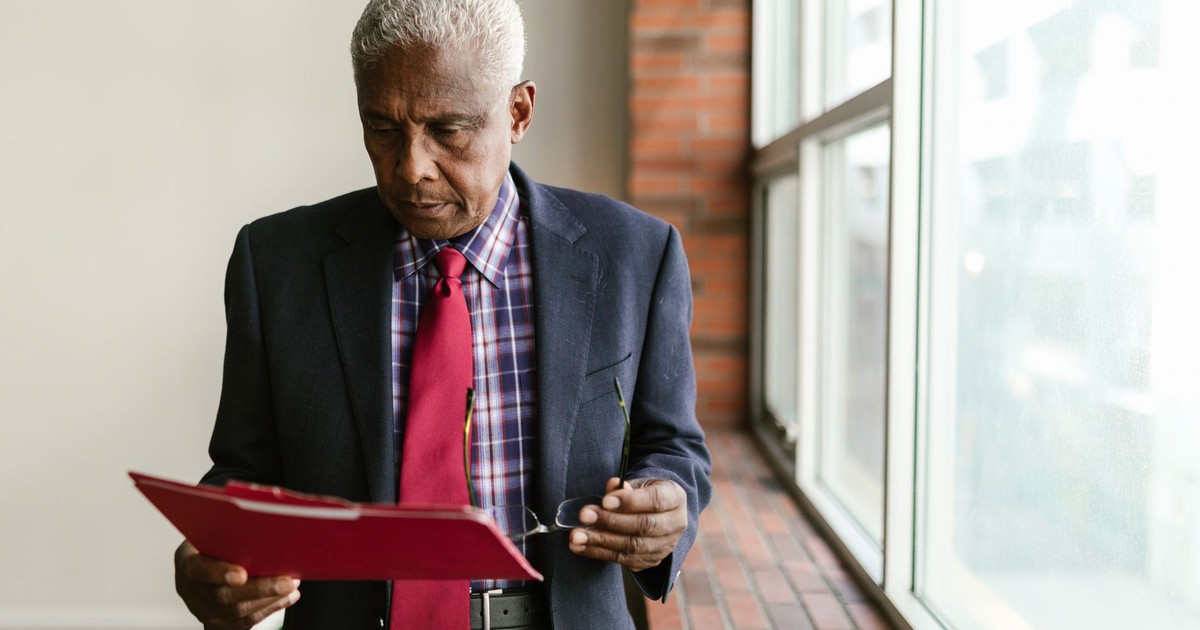 Elderly man in formal attire reviewing documents indoors with natural light.
