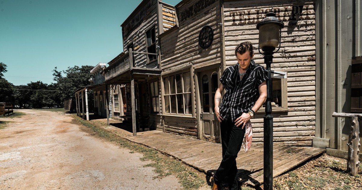 Man in western attire standing on a rustic street in Wimberley, Texas.