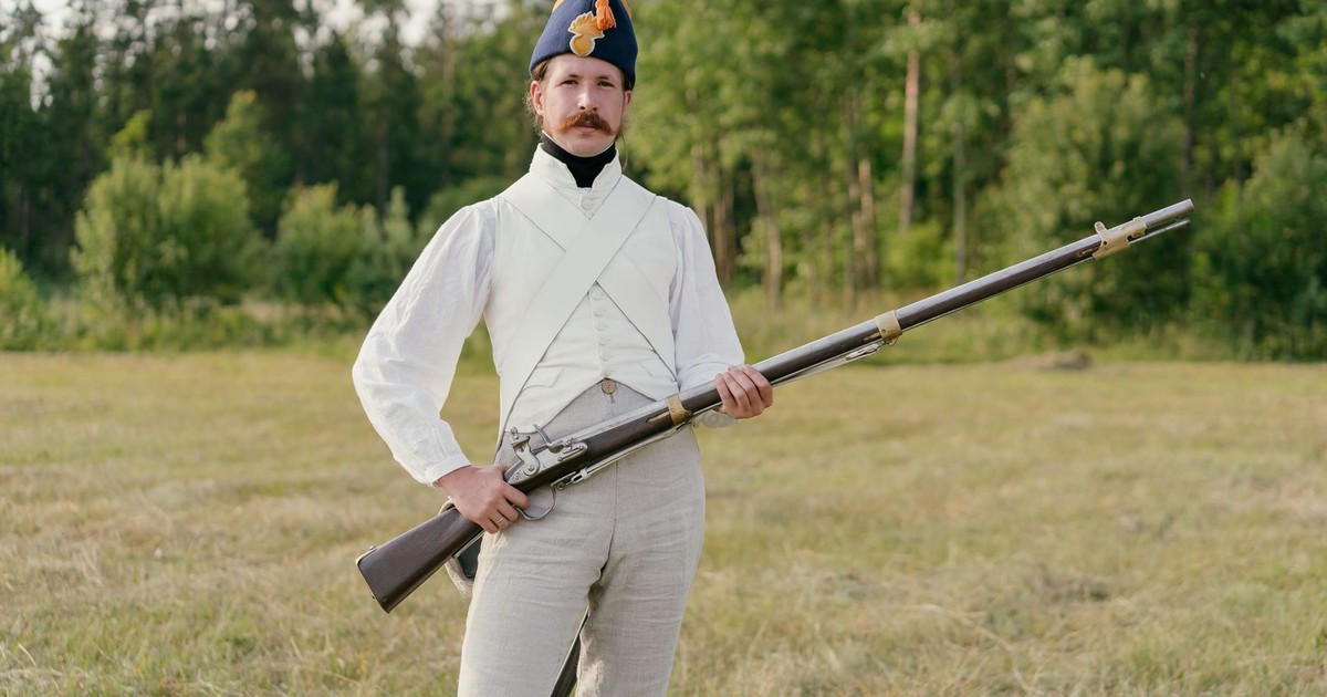 Man dressed in historical uniform with musket in a field setting.