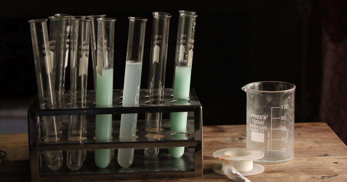 Test tubes and beaker with colorful chemicals on a wooden table in a dim lab.