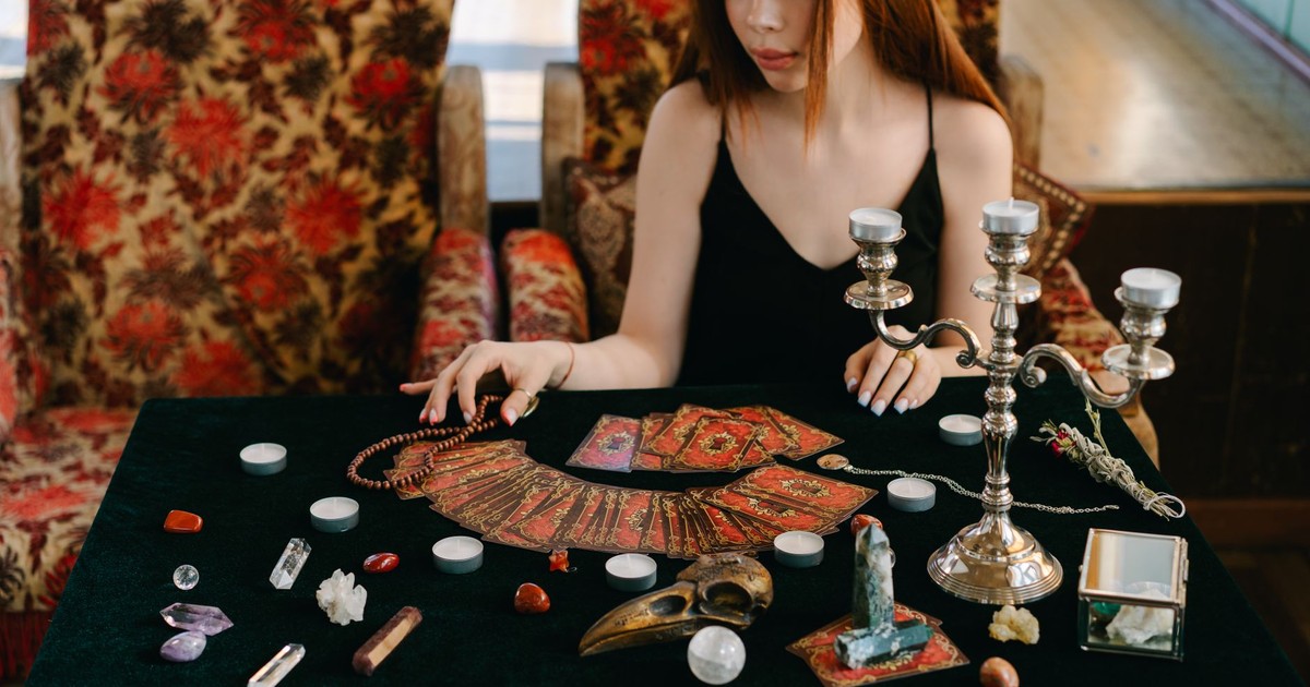 Mystical scene with a woman reading tarot cards surrounded by gemstones and candles.