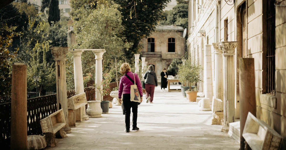 Visitors explore a historic courtyard in Istanbul, capturing the blend of ancient architecture and vibrant greenery on a sunny day.