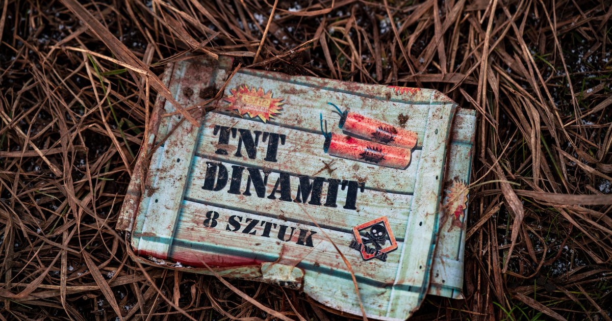 An old TNT box lies on dry grass, showcasing rustic and gritty textures outdoors.