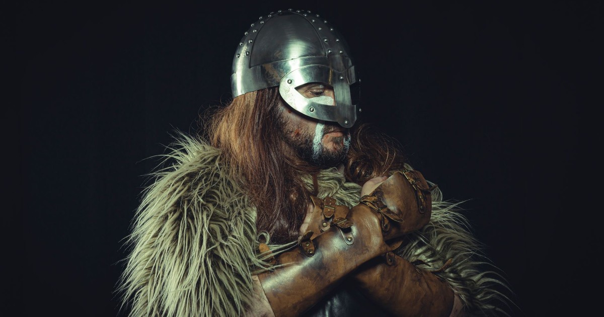 Portrait of a Viking warrior wearing a metal helmet and fur cloak, captured against a dark background.
