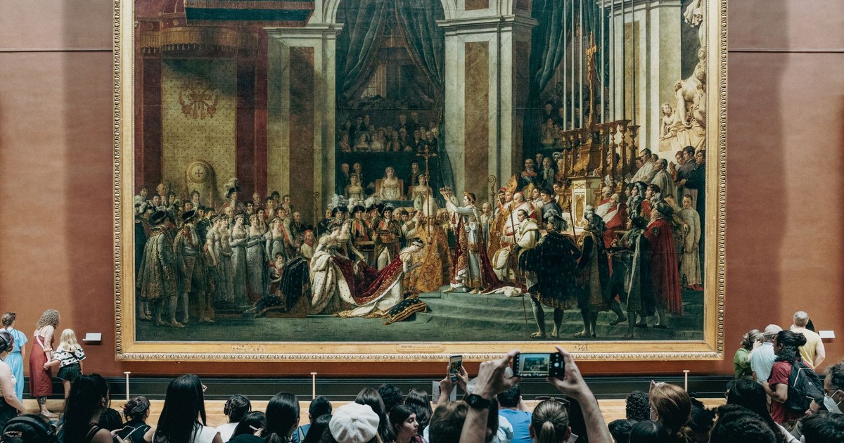 Crowd admires the famous Coronation of Napoleon painting in a gallery setting.