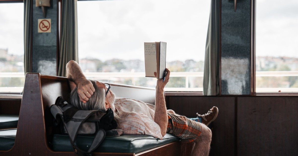 Man relaxing with a book on a train, enjoying the scenic journey through the windows.