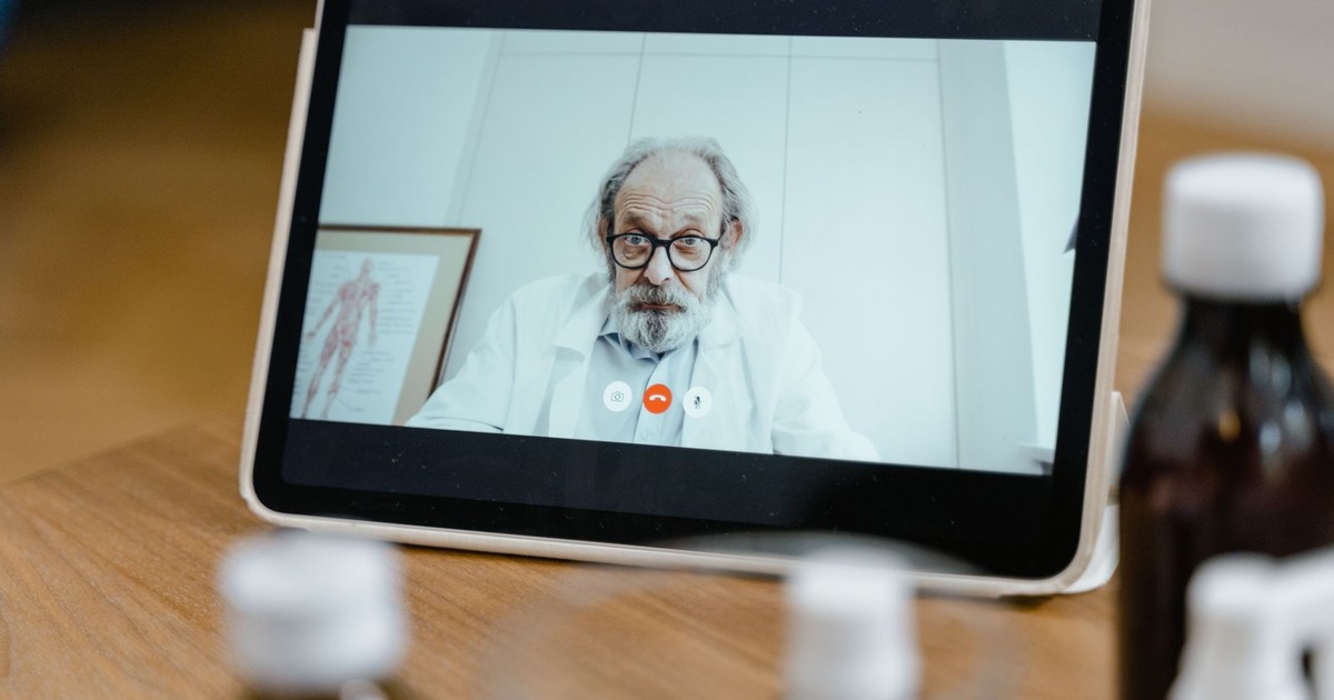 Elderly male doctor in white coat on a digital tablet screen during a virtual medical consultation.